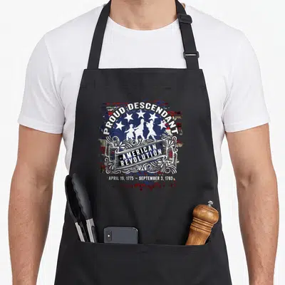 Proud wars classic apron - PROUD DESCENDANT text over soldiers and scrollwork with American Revolution dates — shown on a black cotton canvas apron against a white background