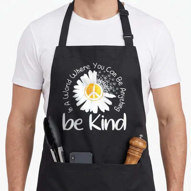 Anything peaceful apron - White daisy with yellow peace symbol core and kindness quote in watercolor style — shown on a black cotton canvas apron against a white background