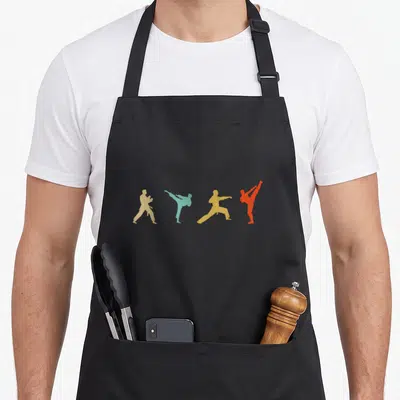 Tae taekwondo apron - Four martial artist silhouettes in beige, teal, yellow, and orange performing kicks and stances — shown on a black cotton canvas apron against a white background