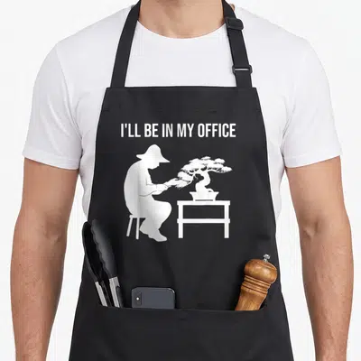 Gardening tree apron - White I'll Be In My Office text above person pruning bonsai silhouette — shown on a black cotton canvas apron against a white background