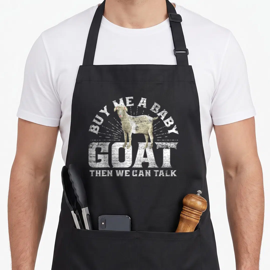 Then goat apron - Distressed white goat with sunburst rays and text BUY ME A BABY GOAT THEN WE CAN TALK — shown on a black cotton canvas apron against a white background