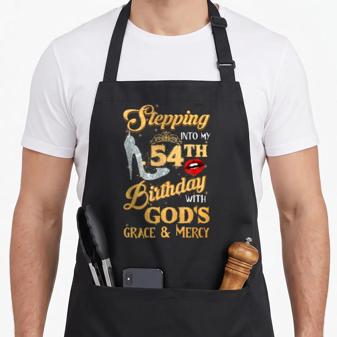 Mercy grace apron - Gold and silver typography Stepping into my 54th Birthday with God's Grace Mercy plus heel and lips — shown on a black cotton canvas apron against a white background