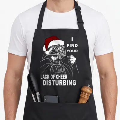 Vader christmas santa apron - Darth Vader wearing a Santa hat with the text I find your lack of cheer disturbing — shown on a black cotton canvas apron against a white background