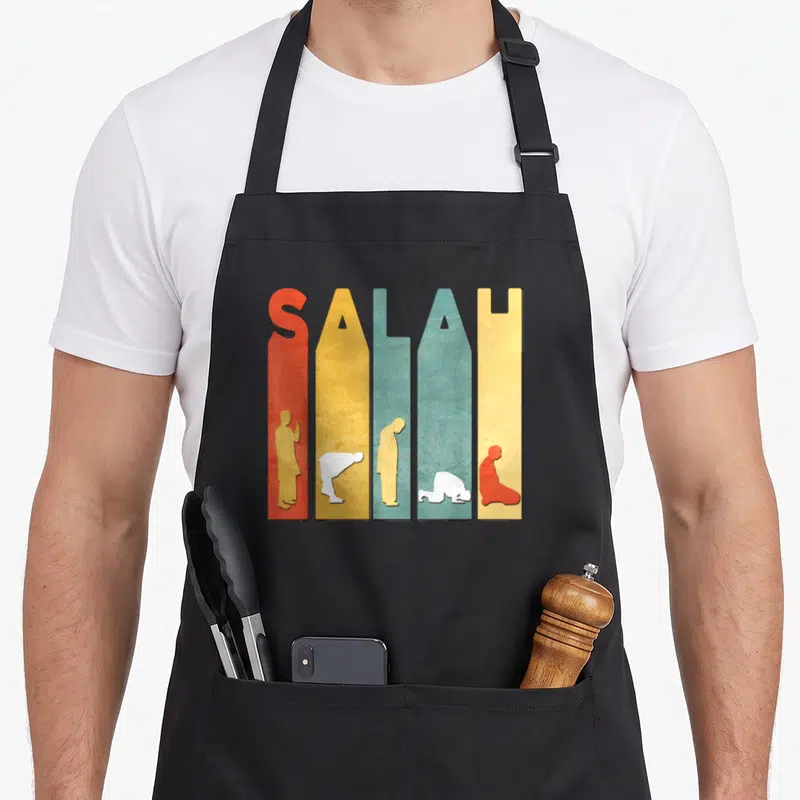 Kareem ramadan apron - SALAH text formed by colored vertical bars containing prayer posture silhouettes — shown on a black cotton canvas apron against a white background