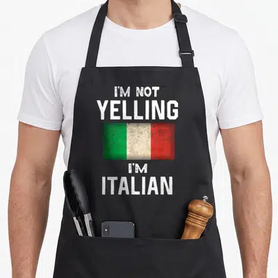 Yelling italy apron - I'M NOT YELLING I'M ITALIAN text above and below green white red flag — shown on a black cotton canvas apron against a white background