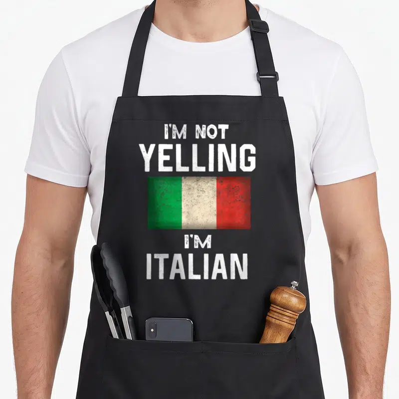 Yelling italy apron - I'M NOT YELLING I'M ITALIAN text above and below green white red flag — shown on a black cotton canvas apron against a white background