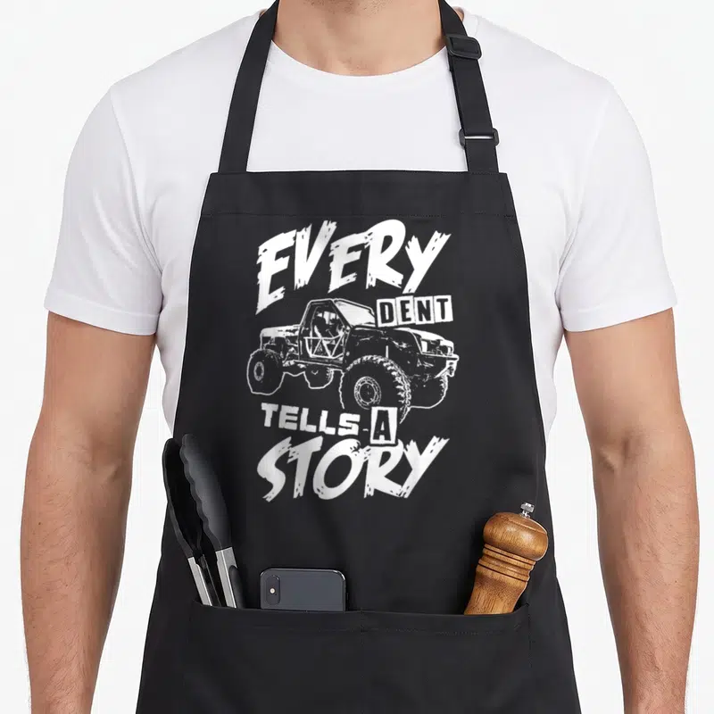 Rock crawler girl apron - Distressed white off-road vehicle with arched text every dent tells a story — shown on a black cotton canvas apron against a white background