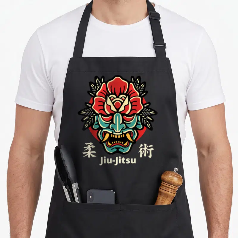 Japanese jiu jitsu apron - Hannya mask with red lotus, teal face, beige Kanji, and Jiu-Jitsu text in line art — shown on a black cotton canvas apron against a white background