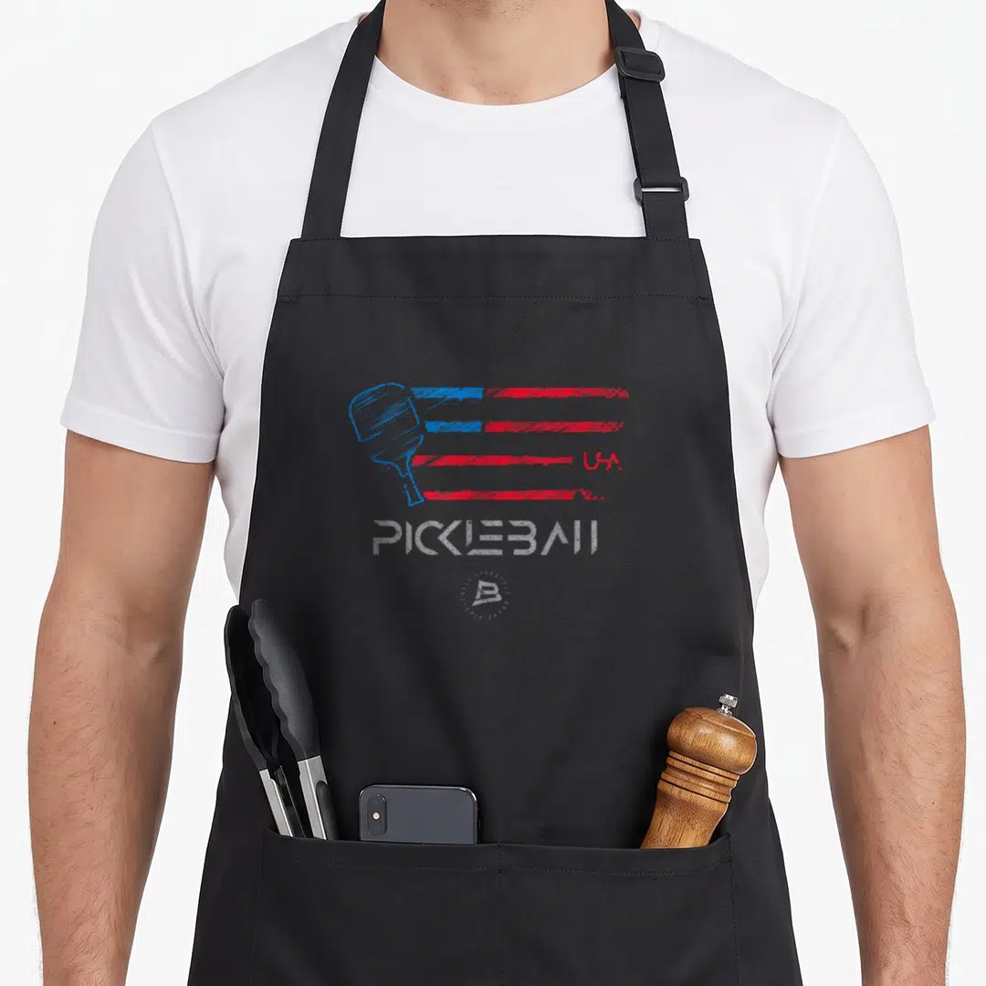 Distressed flag pickleball apron - Pickleball paddle on red and blue stripes with USA and PICKLEBALL text in distressed — shown on a black cotton canvas apron against a white background