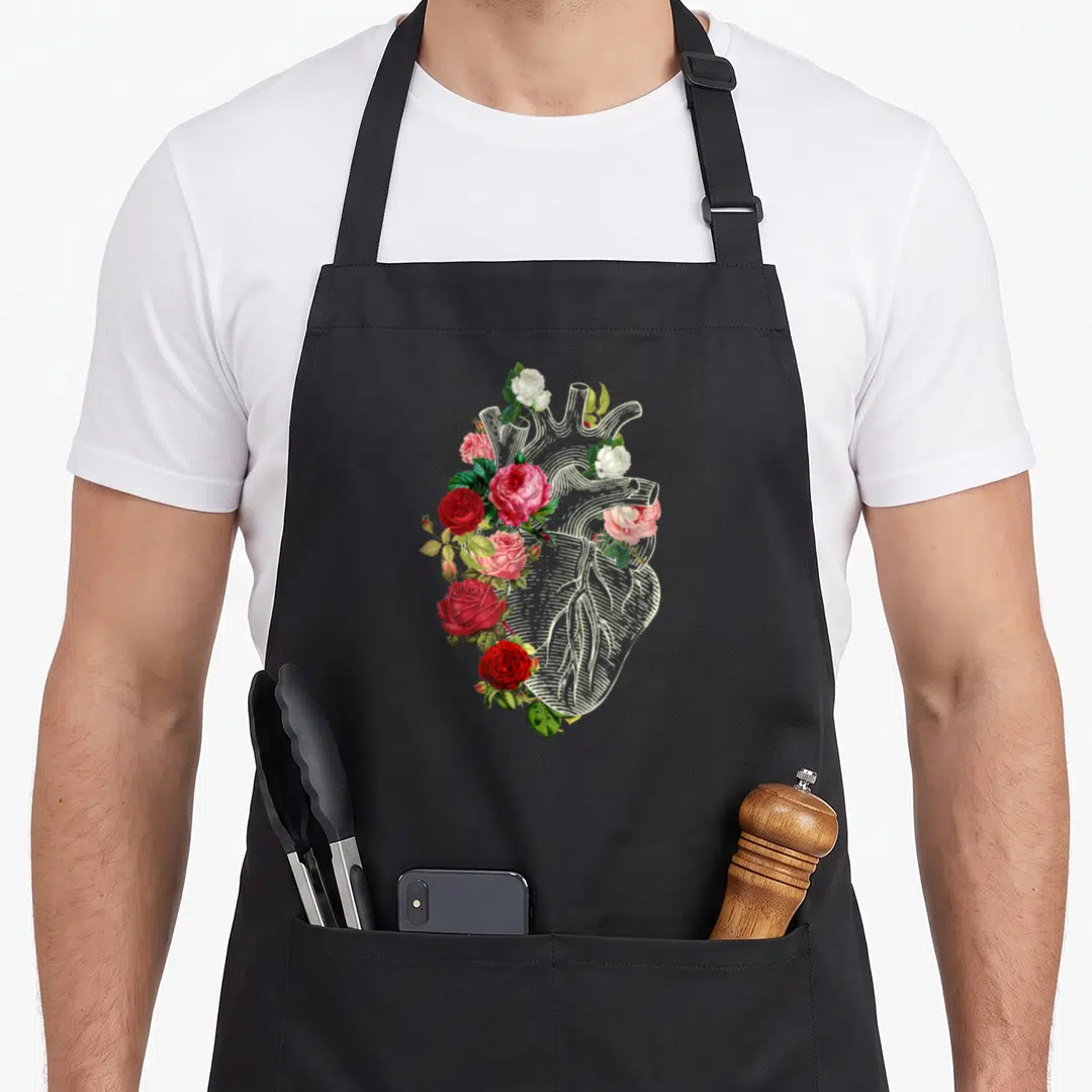 Anatomical nurse apron - White line-art heart surrounded by red pink and white roses with green leaves — shown on a black cotton canvas apron against a white background