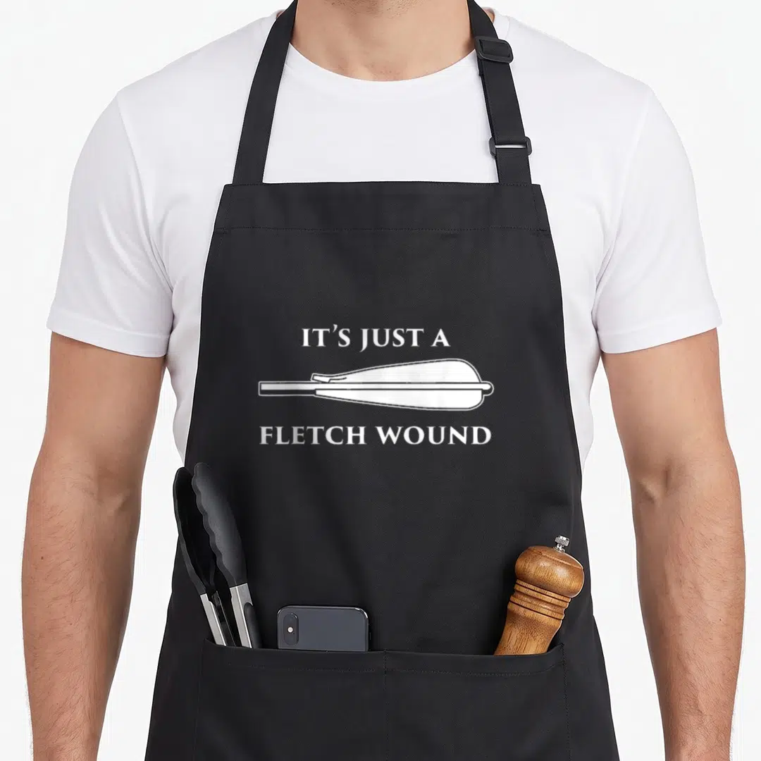 Fletch archery apron - White arrow between IT'S JUST A FLETCH WOUND text — shown on a black cotton canvas apron against a white background