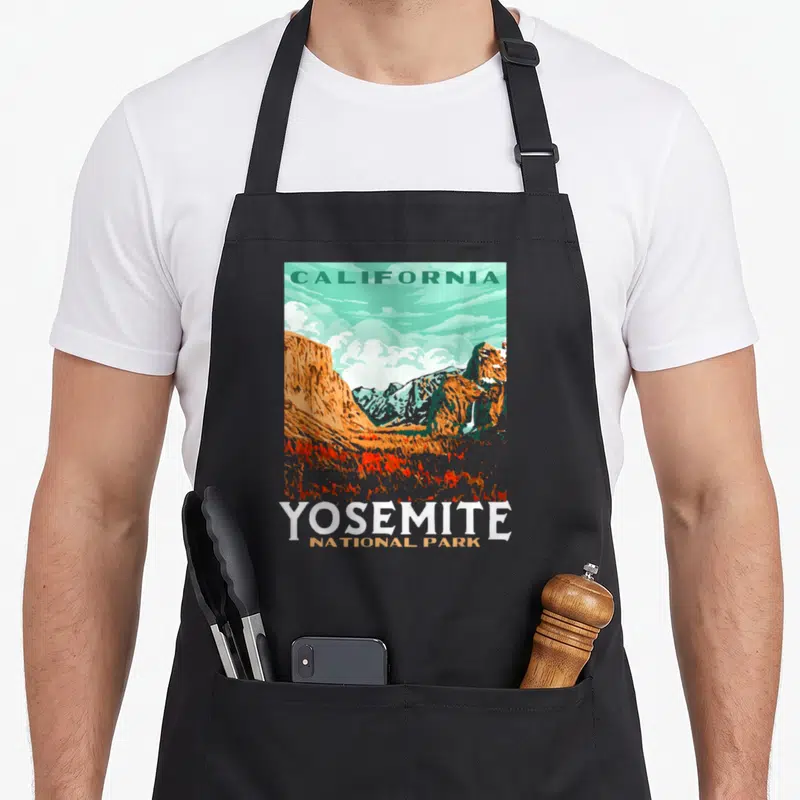Yosemite national park apron - Retro California mountain landscape with waterfall and stacked YOSEMITE NATIONAL PARK — shown on a black cotton canvas apron against a white background