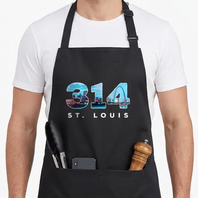 Stl pride apron - 314 area code filled with skyline image and white ST. LOUIS text below — shown on a black cotton canvas apron against a white background