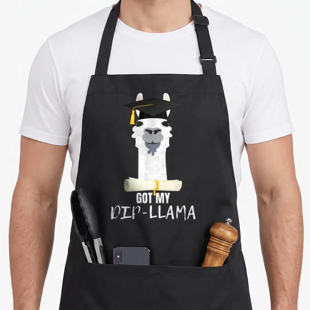 Dip funny graduation apron - White llama in black cap holding diploma scroll with GOT MY DIP-LLAMA text — shown on a black cotton canvas apron against a white background