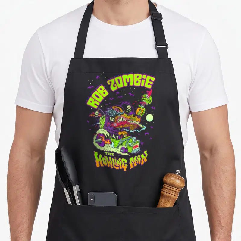 Howling zombie apron - Cartoon werewolf driving green hot rod with ROB ZOMBIE text and purple bats — shown on a black cotton canvas apron against a white background