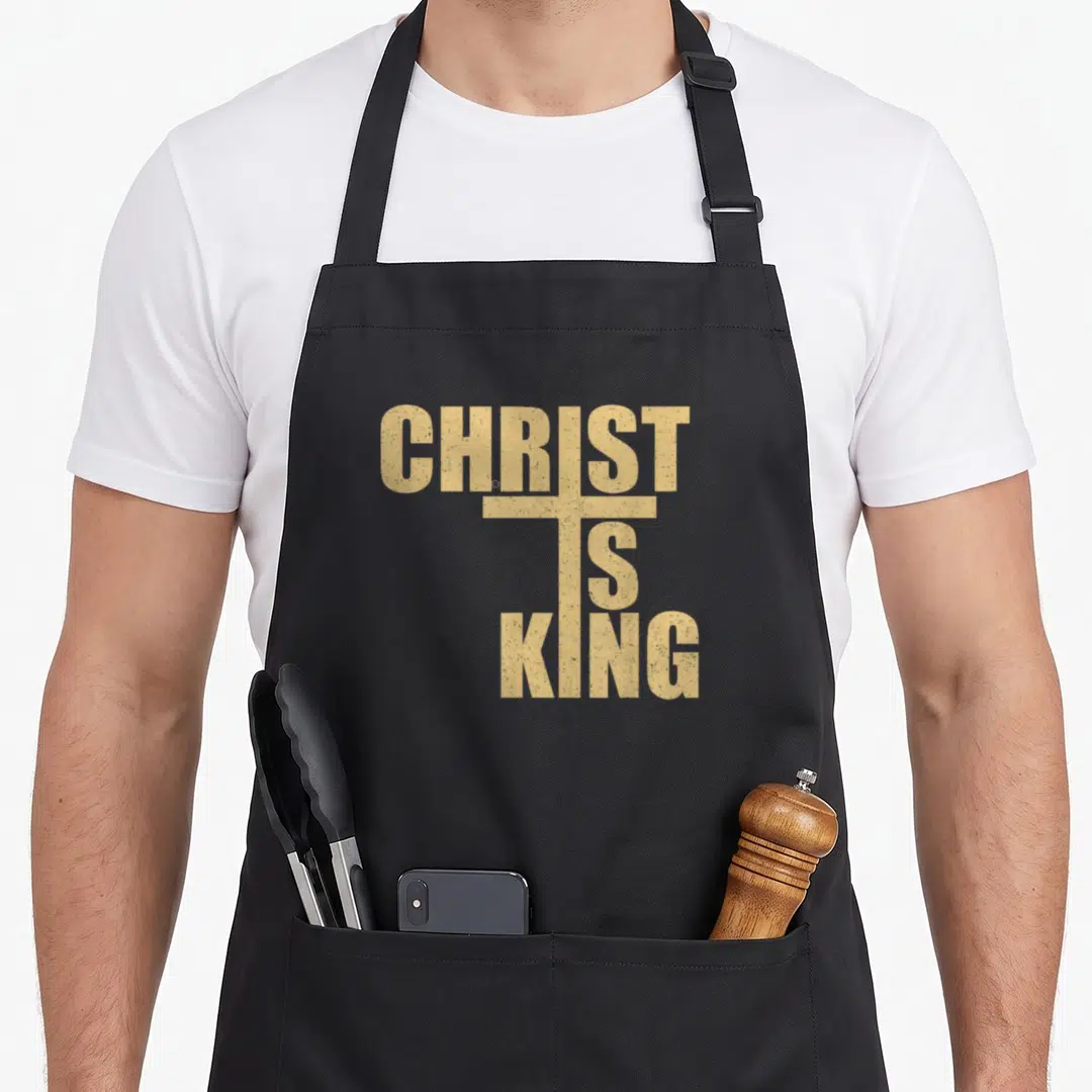 King cross apron - Tan distressed text CHRIST IS KING stacked to form a cross shape — shown on a black cotton canvas apron against a white background