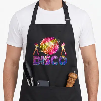 Disco theme 70s apron - Colorful disco ball graphic with two dancers and DISCO text in pink yellow blue purple — shown on a black cotton canvas apron against a white background