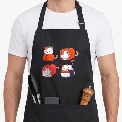 Persian sushi cat apron - Four cartoon cats styled as sushi fillings in white orange red and purple grid — shown on a black cotton canvas apron against a white background