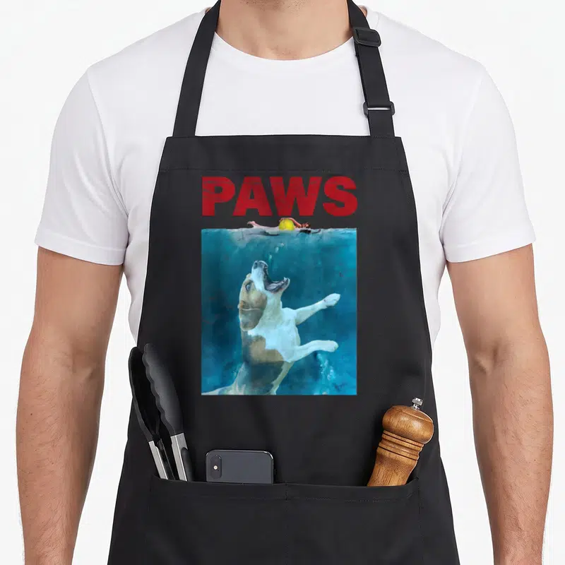 Underwater beagle apron - PAWS text above photo of brown and white dog leaping underwater — shown on a black cotton canvas apron against a white background