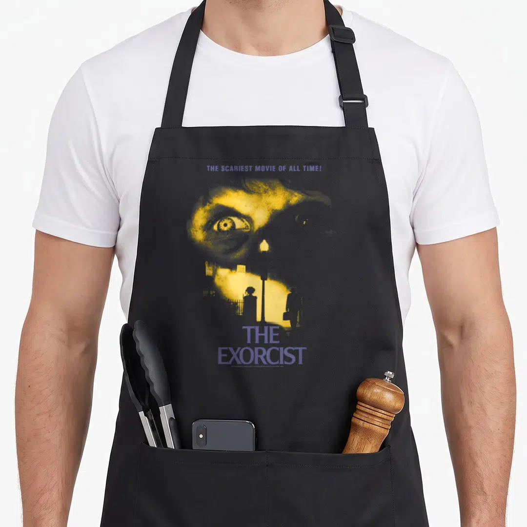 Exorcist movie poster apron - Yellow stylized face with purple text reading The Exorcist and scariest movie quote — shown on a black cotton canvas apron against a white background