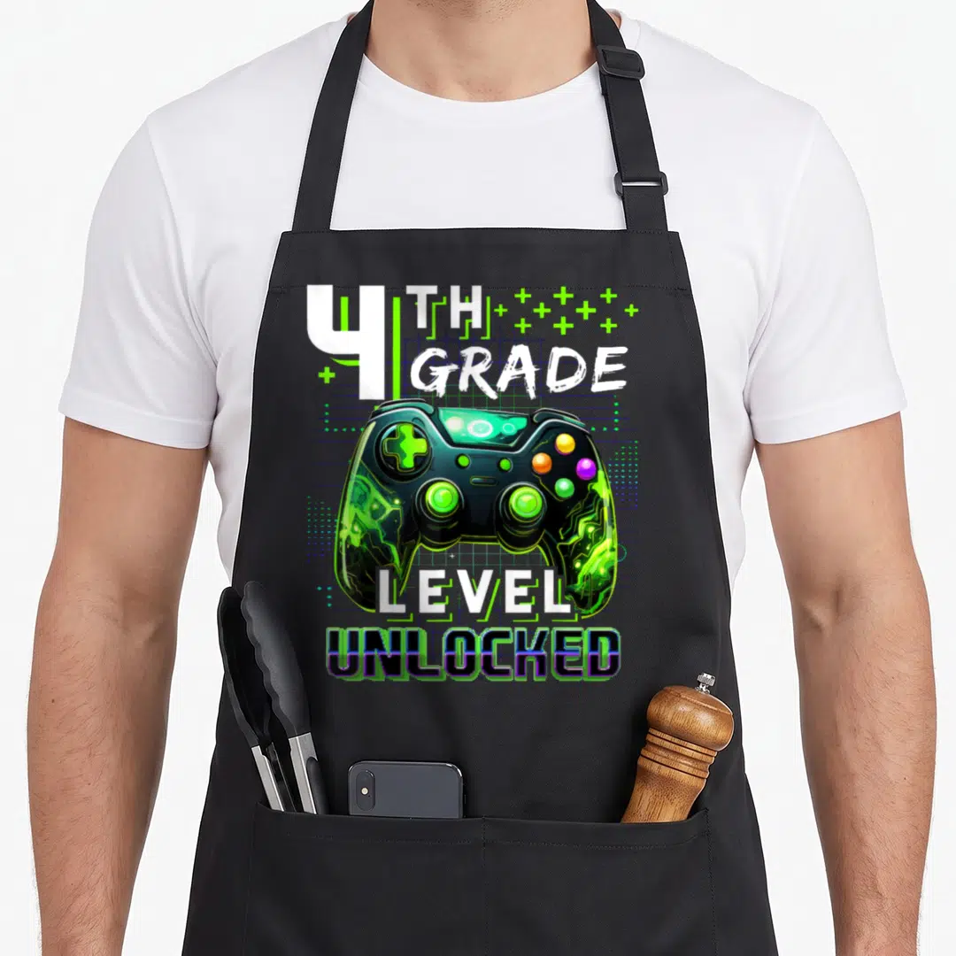 4th level apron - Game controller with 4th grade level unlocked text and green plus signs — shown on a black cotton canvas apron against a white background