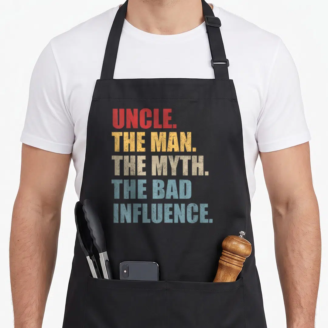Myth funcle apron - Stacked red yellow beige and blue text reading Uncle The Man The Myth The Bad Influence — shown on a black cotton canvas apron against a white background