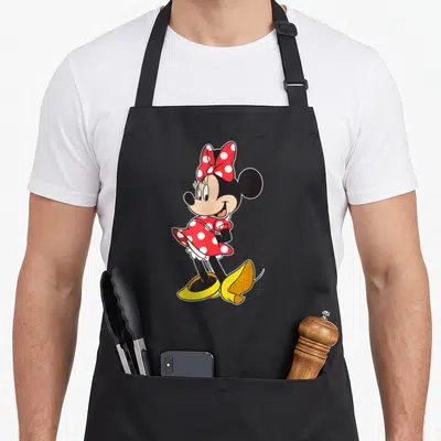 Pose mouse apron - Minnie Mouse in red polka dot dress and yellow shoes standing in a cartoon pose — shown on a black cotton canvas apron against a white background