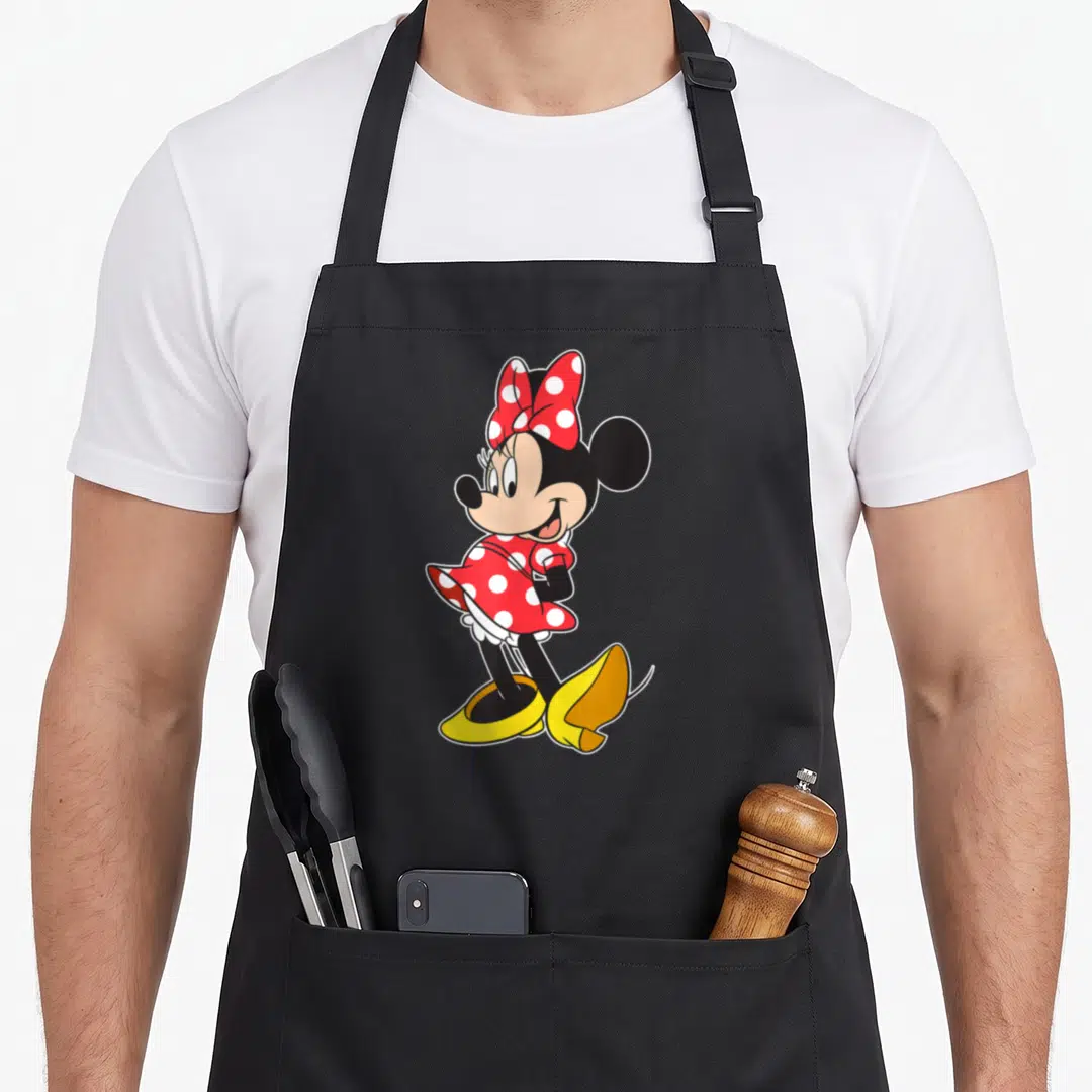 Pose mouse apron - Minnie Mouse in red polka dot dress and yellow shoes standing in a cartoon pose — shown on a black cotton canvas apron against a white background