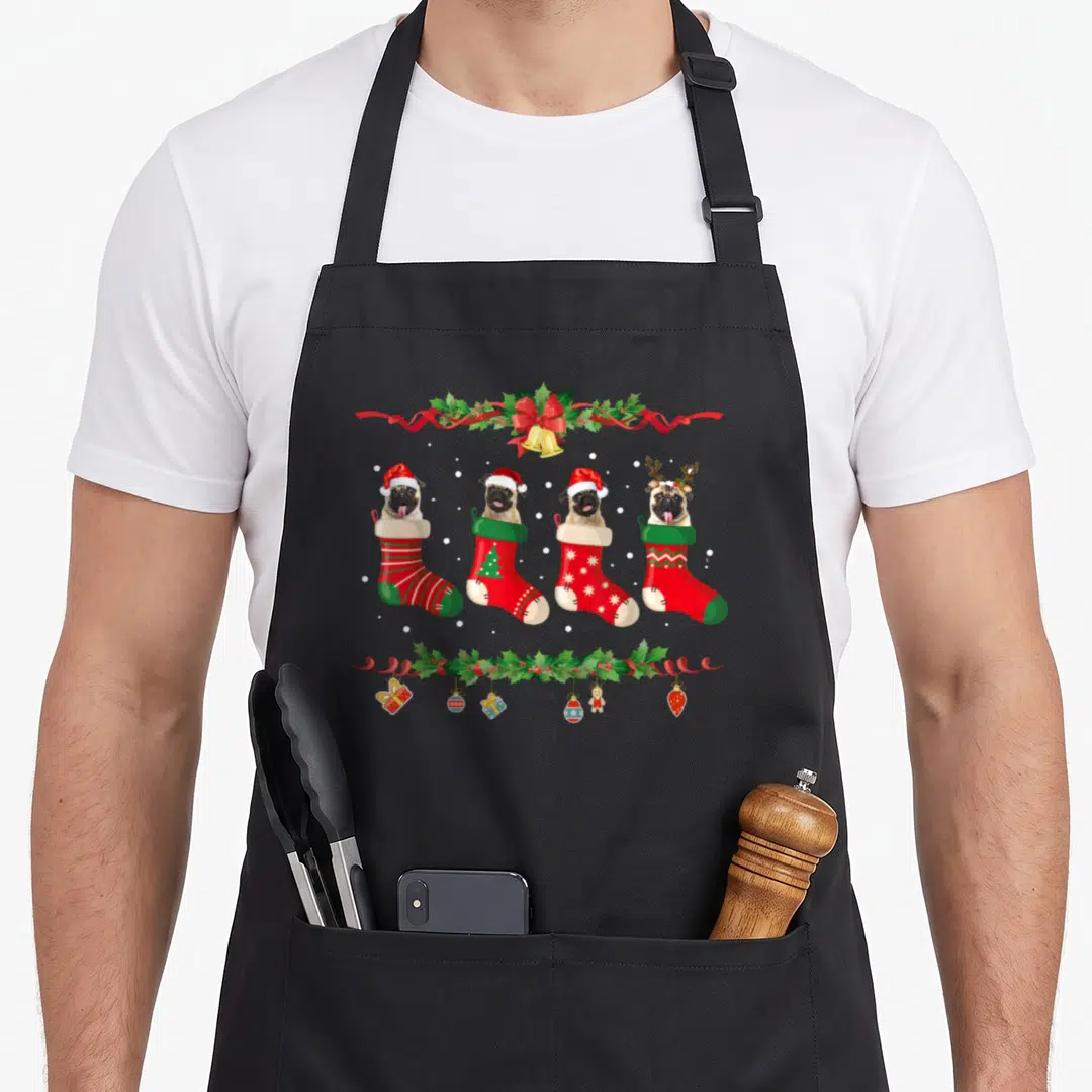 Dog womens christmas aprons - Four pugs in stockings between holly borders with hanging ornaments and gifts — shown on a black cotton canvas apron against a white background