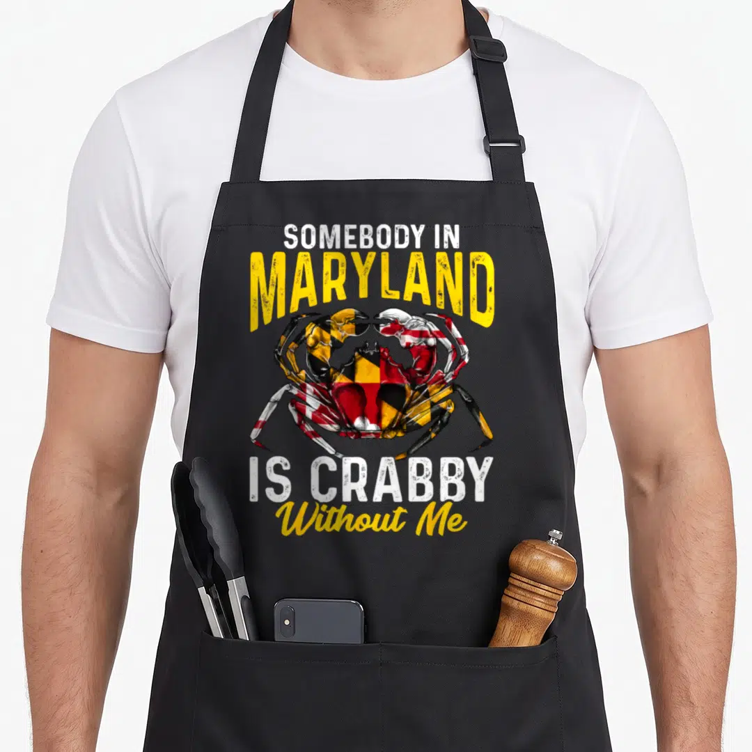 Somebody crab apron - Realistic crab with Maryland flag colors and text SOMEBODY IN MARYLAND IS CRABBY Without Me — shown on a black cotton canvas apron against a white background