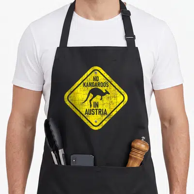 Zookeeper kangaroo apron - Yellow diamond sign with black border, kangaroo silhouette, and text No Kangaroos in Austria — shown on a black cotton canvas apron against a white background