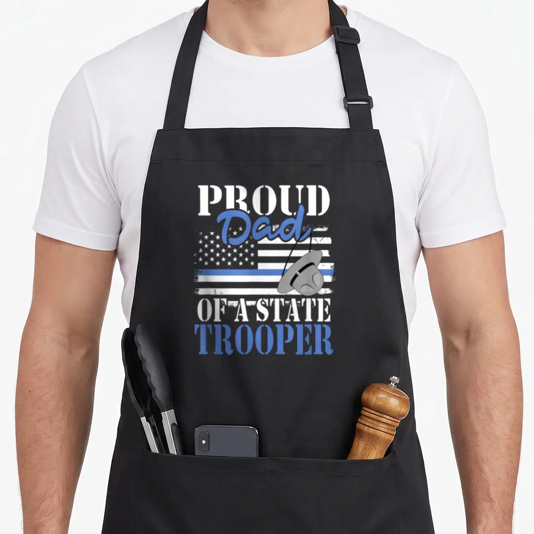 State police apron - Distressed flag with blue line, grey trooper hat, and proud dad text — shown on a black cotton canvas apron against a white background