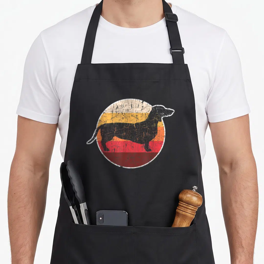 Mother dog dad apron - Grey dachshund silhouette over retro yellow orange red and maroon stripes — shown on a black cotton canvas apron against a white background