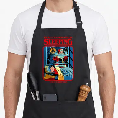 Steven santa claus apron - Red text He Sees You When You're Sleeping above cartoon Santa peeking through window — shown on a black cotton canvas apron against a white background