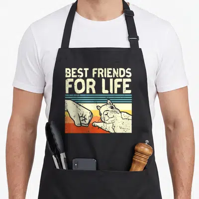 Fist friends apron - Best Friends For Life text above human fist bumping guinea pig paw over blue yellow orange red — shown on a black cotton canvas apron against a white background