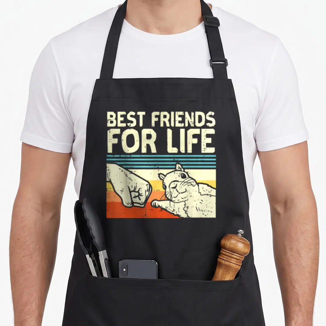 Fist friends apron - Best Friends For Life text above human fist bumping guinea pig paw over blue yellow orange red — shown on a black cotton canvas apron against a white background
