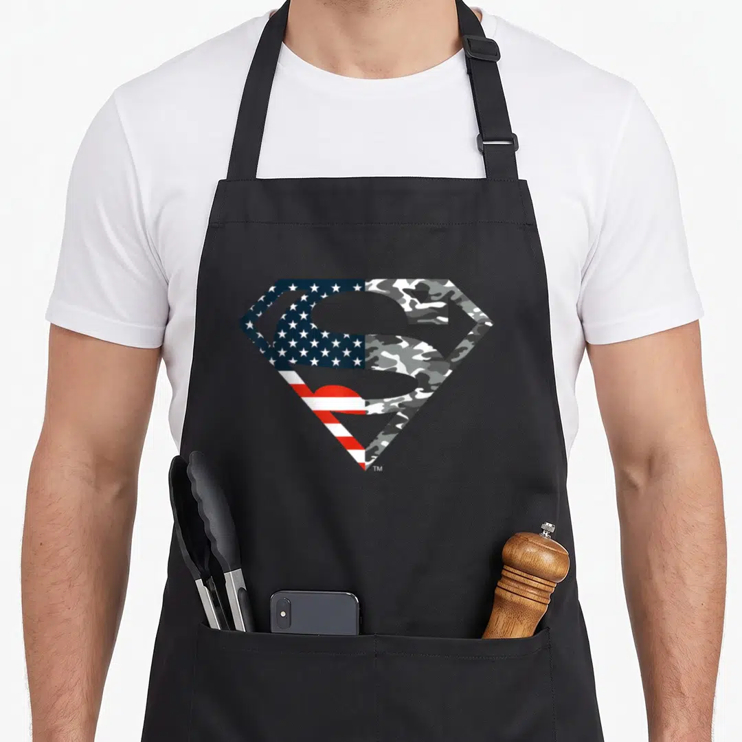 Funny flag camo aprons - Split Superman shield with US flag left and grey camo right — shown on a black cotton canvas apron against a white background
