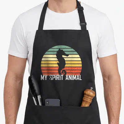 Seahorse animal apron - Grey seahorse silhouette over green yellow orange red striped sun with My Spirit Animal text — shown on a black cotton canvas apron against a white background