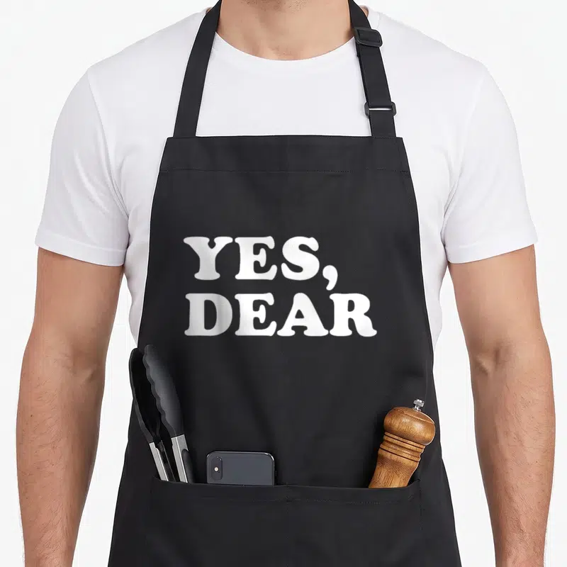 Dear valentine's day apron - White stacked typography reading yes, dear on a dark background — shown on a black cotton canvas apron against a white background