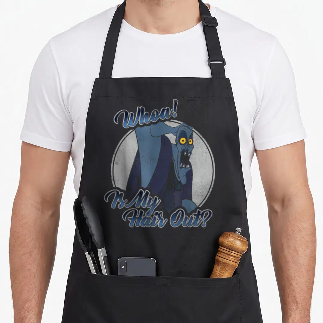 Hercule hair apron - Blue cartoon character with yellow eyes and text Whoa Is My Hair Out inside grey circle — shown on a black cotton canvas apron against a white background