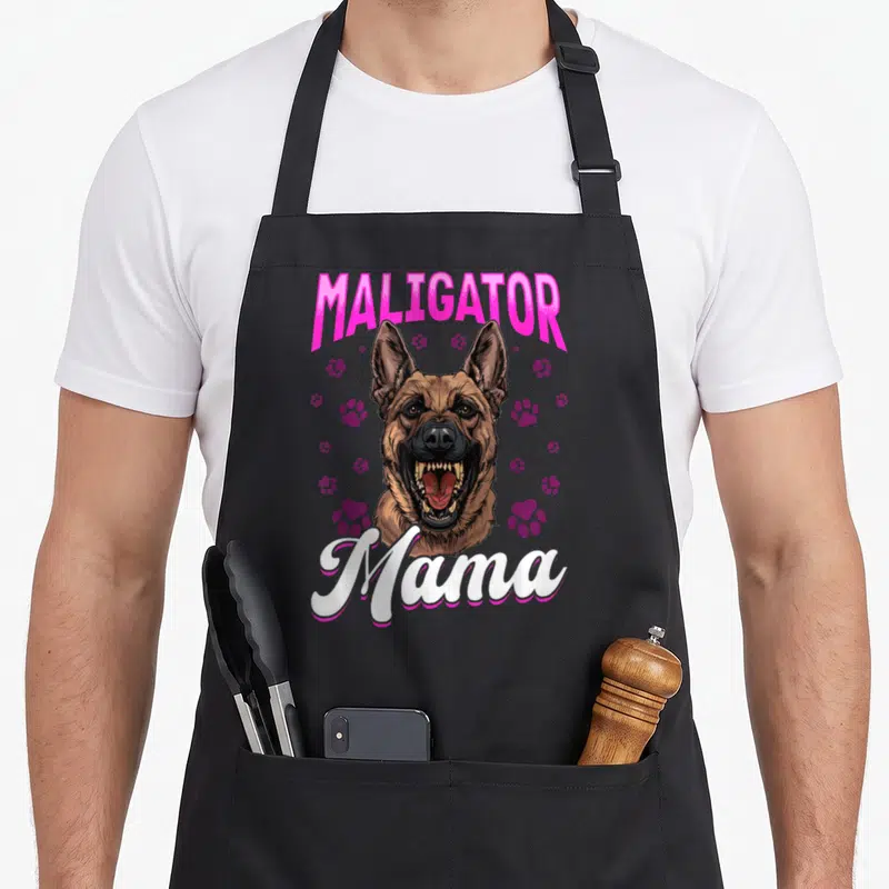 Maligator dog breed aprons - Cartoon Belgian Malinois with pink MALIGATOR text and purple paw prints — shown on a black cotton canvas apron against a white background