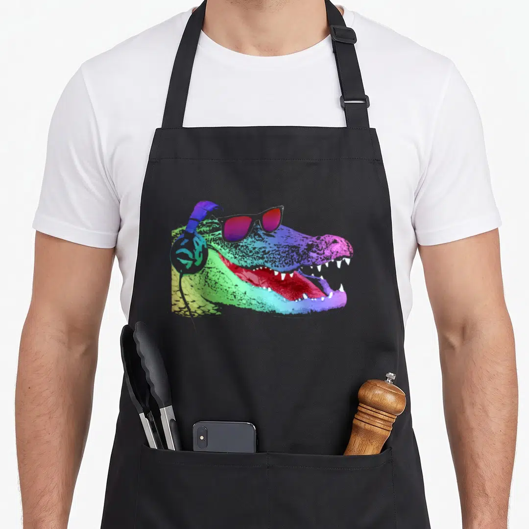 Headphone alligator apron - Rainbow crocodile head in profile with sunglasses and headphones in cartoon style — shown on a black cotton canvas apron against a white background