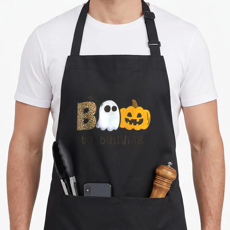 Boo unity day apron - Leopard B, white ghost, orange pumpkin spelling Boo with spider web and text to bullying — shown on a black cotton canvas apron against a white background