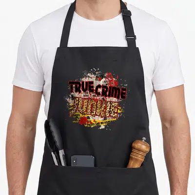 Junki leopard print apron - TRUE CRIME JUNKIE text with leopard print fill, yellow police tape, and red blood splatters — shown on a black cotton canvas apron against a white background