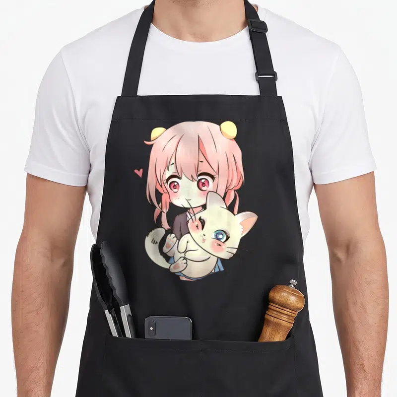 Manga kawaii cooking apron - Pink haired girl holding white cat with floating heart cartoon art — shown on a black cotton canvas apron against a white background