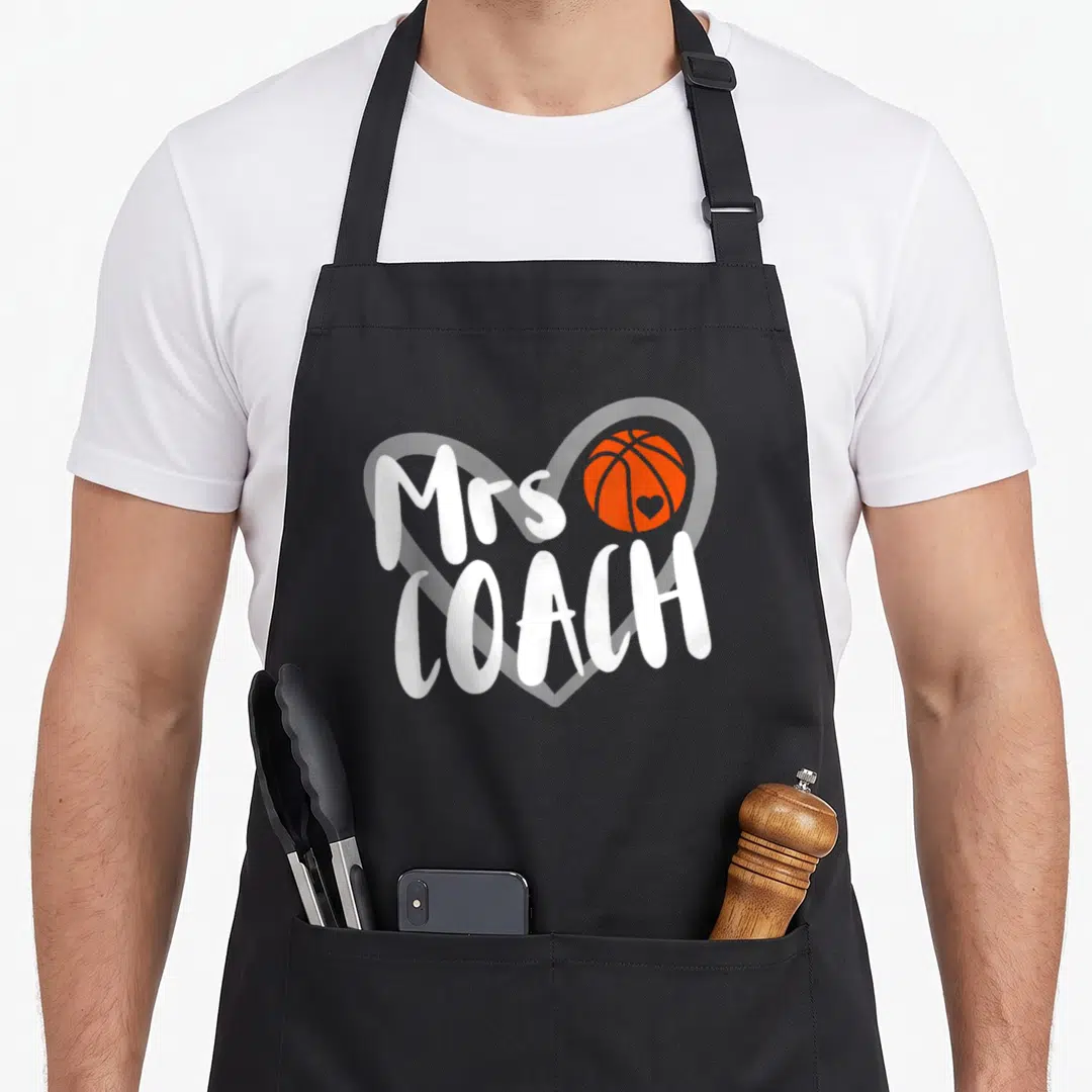 Basketball coach wife apron - Mrs COACH text over white heart outline with orange basketball containing small heart — shown on a black cotton canvas apron against a white background