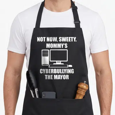 Sweety mayor apron - White text NOT NOW SWEETY MOMMYS CYBERBULLYING THE MAYOR around a computer icon on black fabric — shown on a black cotton canvas apron against a white background