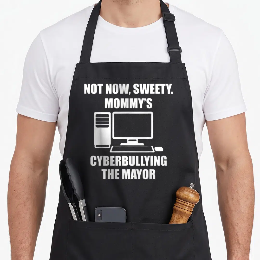 Sweety mayor apron - White text NOT NOW SWEETY MOMMYS CYBERBULLYING THE MAYOR around a computer icon on black fabric — shown on a black cotton canvas apron against a white background