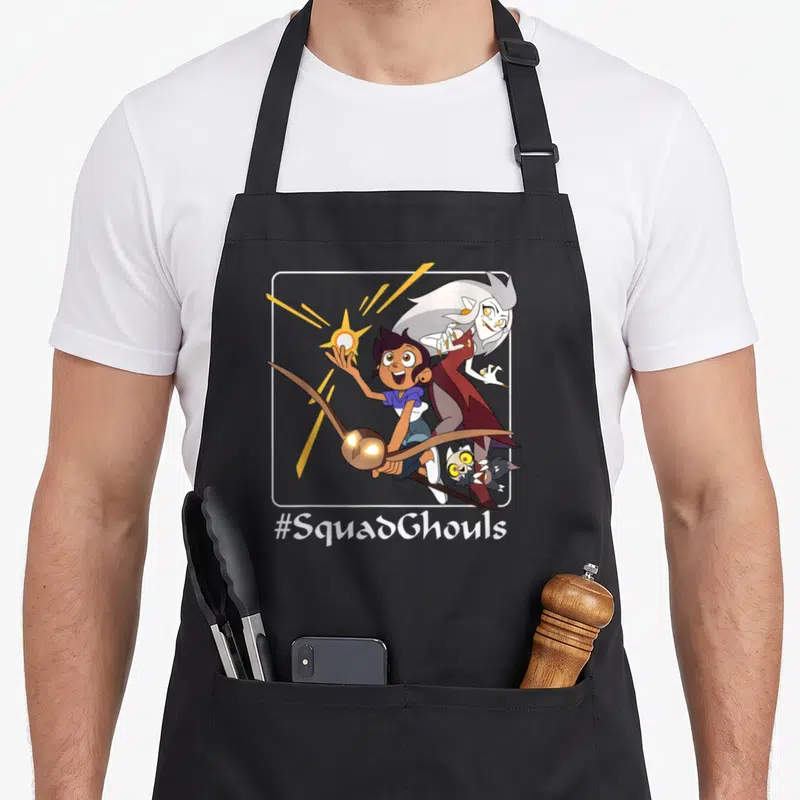 Squadghoul owl apron - Three cartoon characters in white frame with yellow orb and #SquadGhouls text — shown on a black cotton canvas apron against a white background