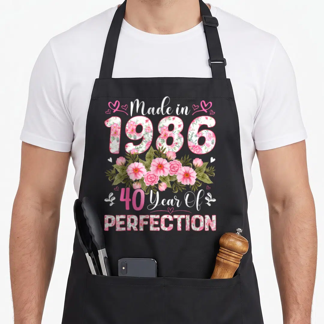 40th vintage floral apron - Floral 1986 text stack with pink roses and 40 Year Of Perfection message — shown on a black cotton canvas apron against a white background